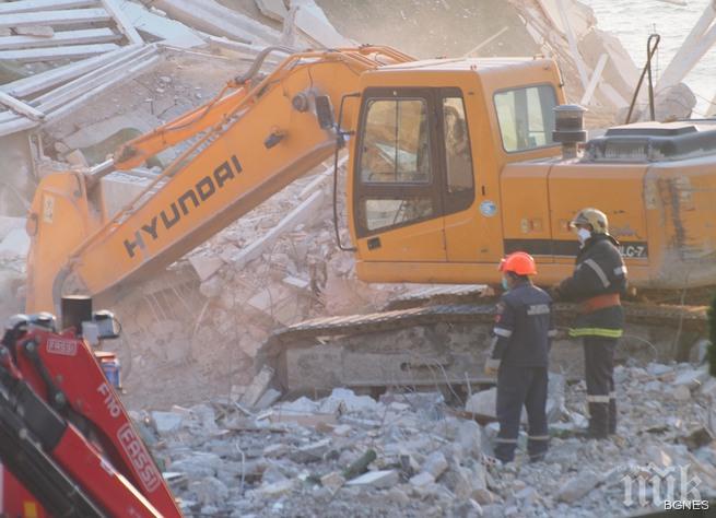 Оцелял работник със скъсани дрехи помага в разчистването на отломките